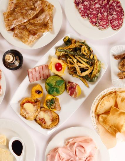 Antipasti caldi, salumi e gnocco fritto della Trattoria La Busa disposti sulla tavola, vista verticale.