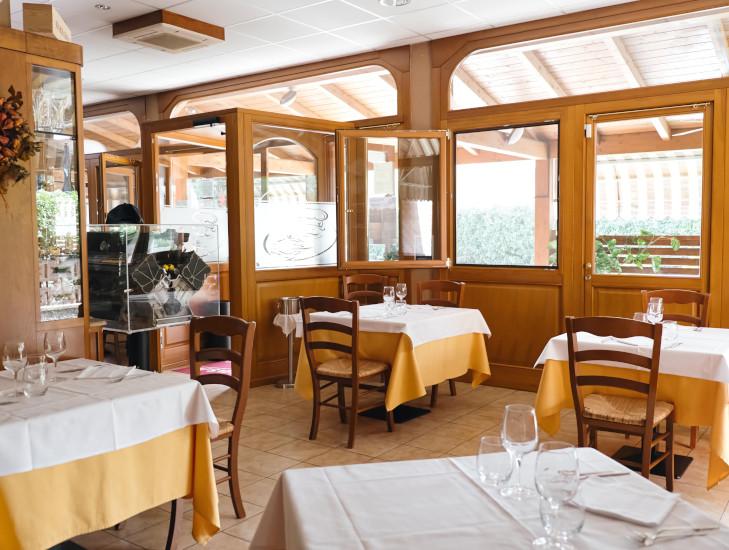 Sala interna luminosa dell'Antica Trattoria La Busa a Spilamberto, con tavoli apparecchiati e arredi in legno.